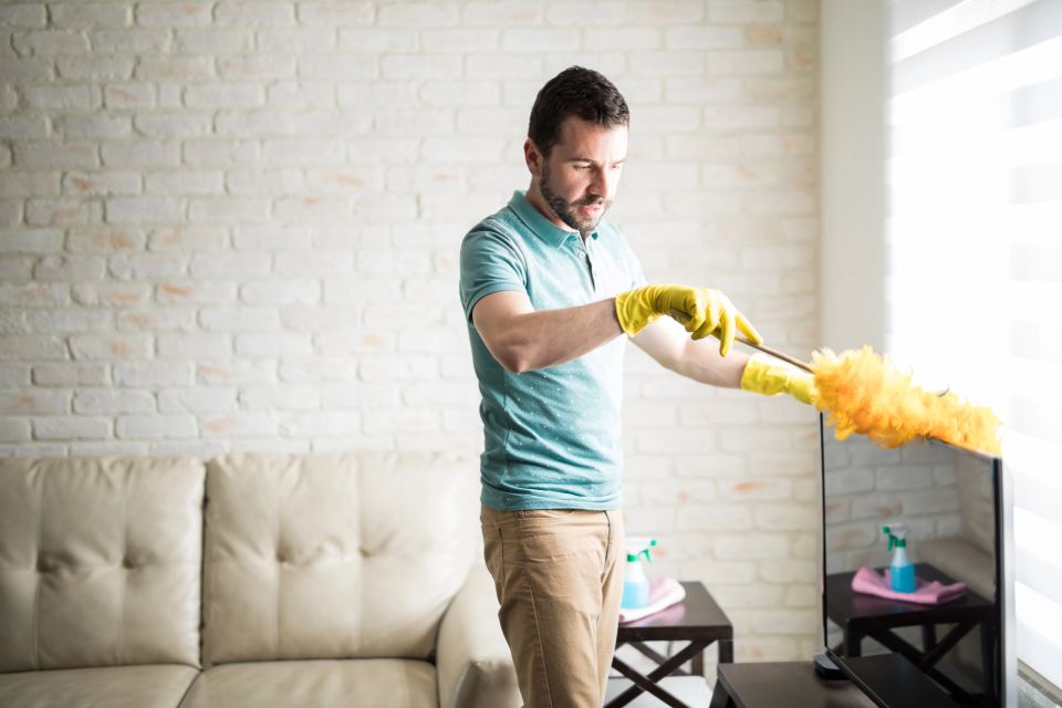 A man wearing yellow gloves dusting his living room TV area