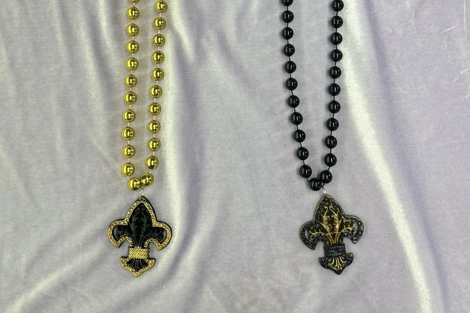 A gold bead with a black fleur de lis emblem outlined in gold and a black bead with a black fleur de lis emblem with gold accents