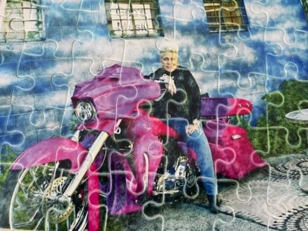 Custom jigsaw puzzle featuring Kelly Morocco seated on a bright pink motorcycle against a blue wall backdrop.