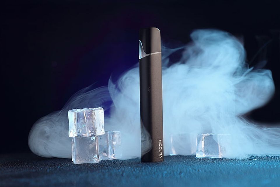 Black vape pen beside ice cubes with rising mist