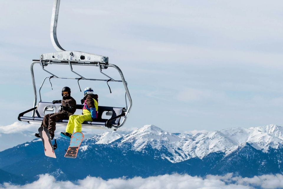 Two snowboarders on a chair lift with a mountain range behind them