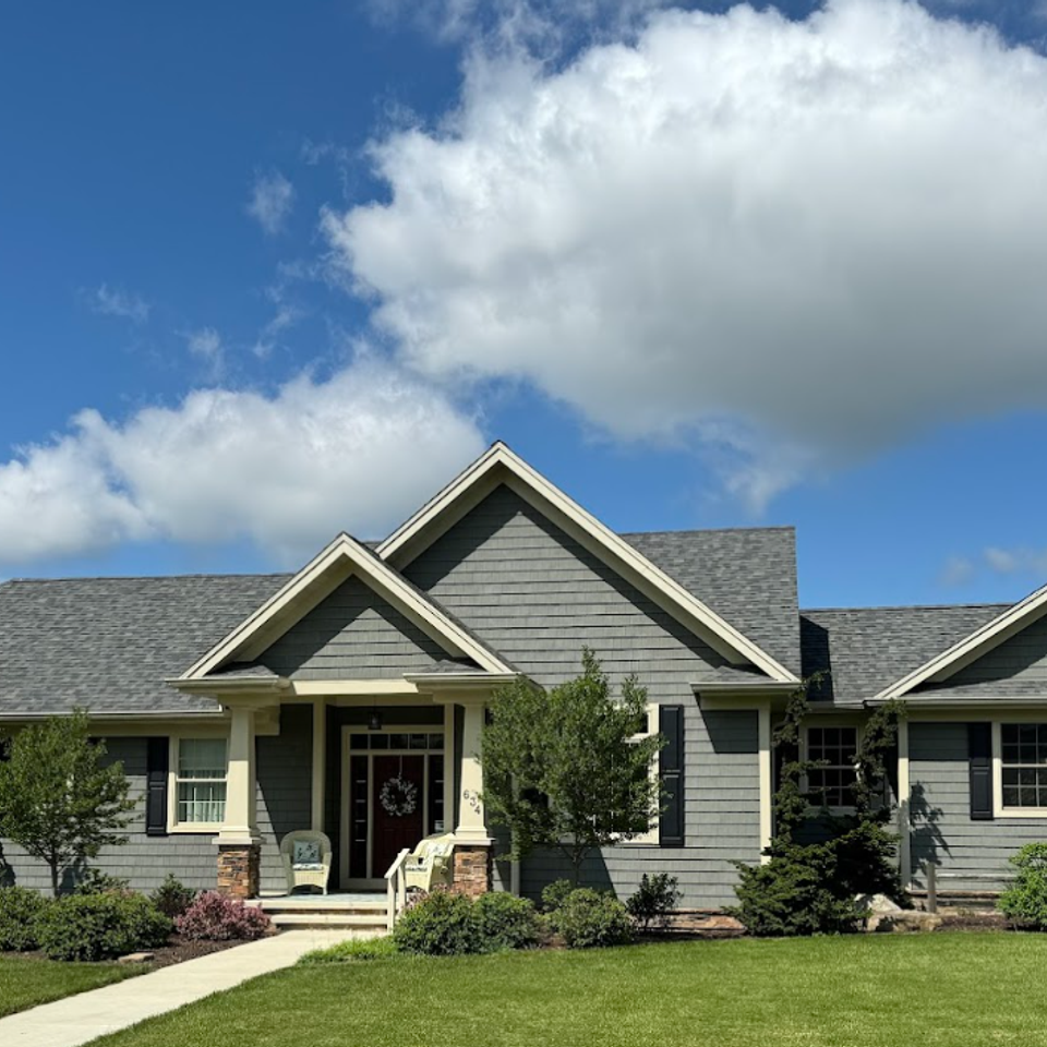 Completed custom home featuring gray siding, multiple front-facing gables, a covered entryway, and professionally landscaped grounds.