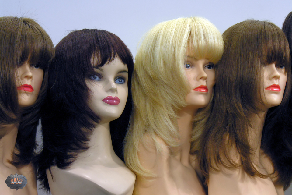 Mannequin heads displaying wigs in brunette, black, and blonde shades with layered styles and bangs inside Shears Wigs & Hairpieces Salon.
