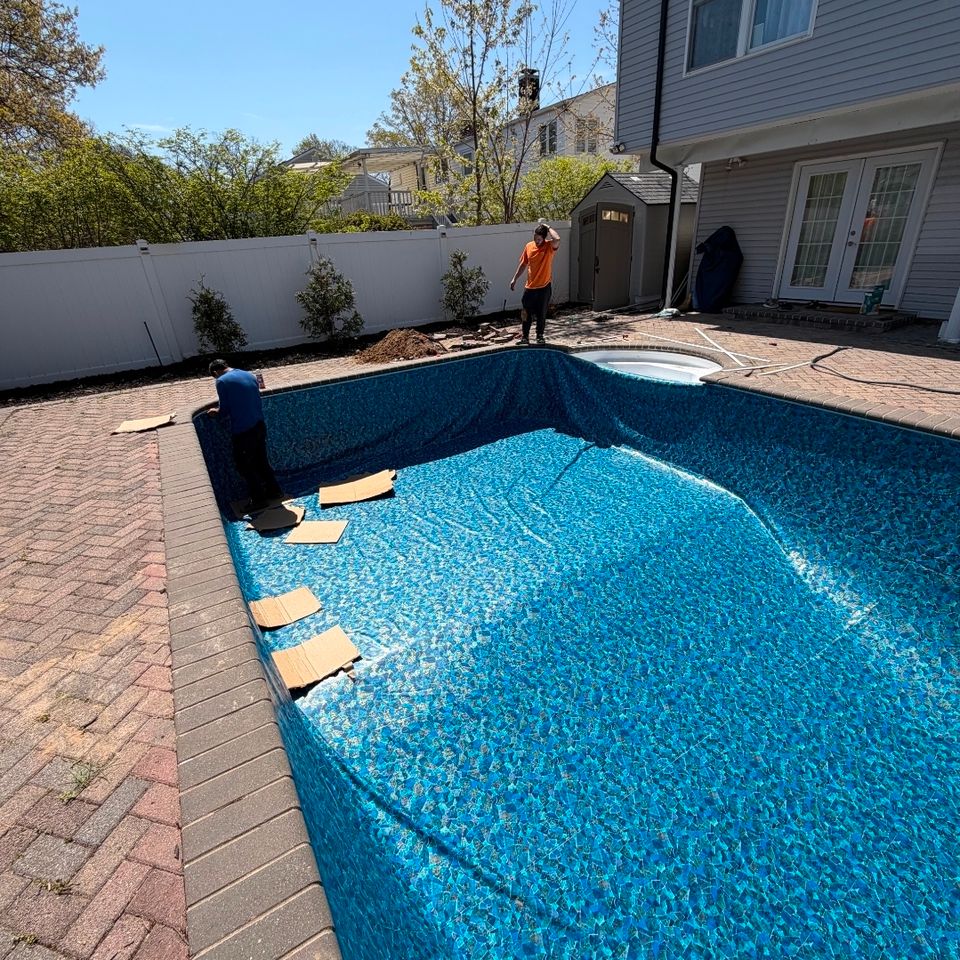 Crew smoothing a new mosaic pattern liner in an inground pool with attached spa