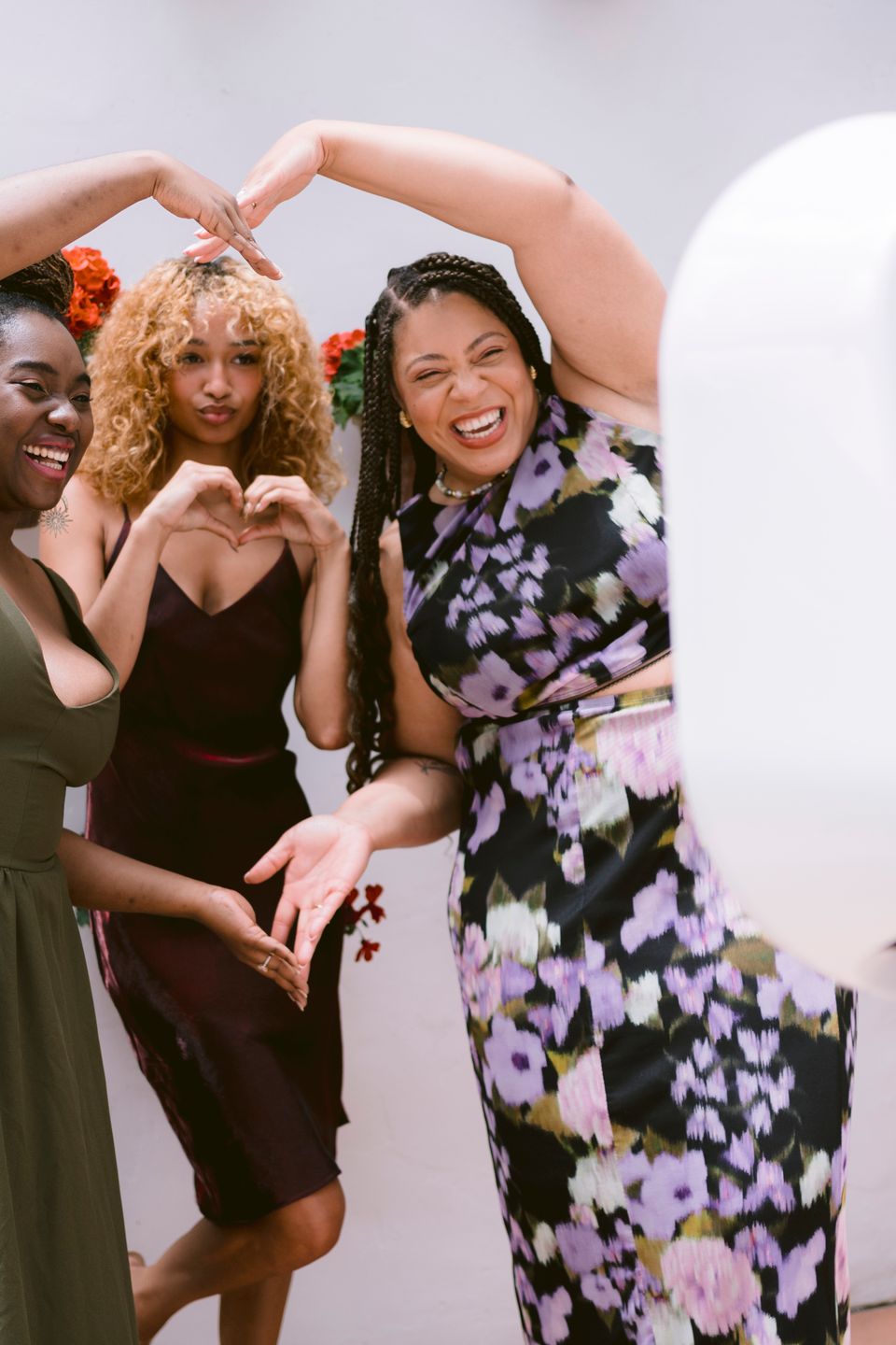 Three women posing with heart hand gestures in front of a digital photo booth.