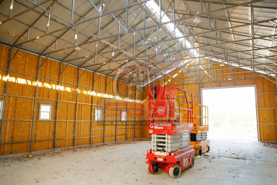 Interior of steel building under construction with lift equipment and framing with SBSI watermark representing steel building interiors in Alabama
