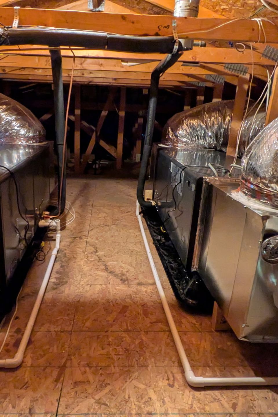 Dual high-efficiency HVAC air handlers installed in an attic with insulated flexible duct-work, organized condensate drain lines, and professionally routed components for residential heating and cooling.