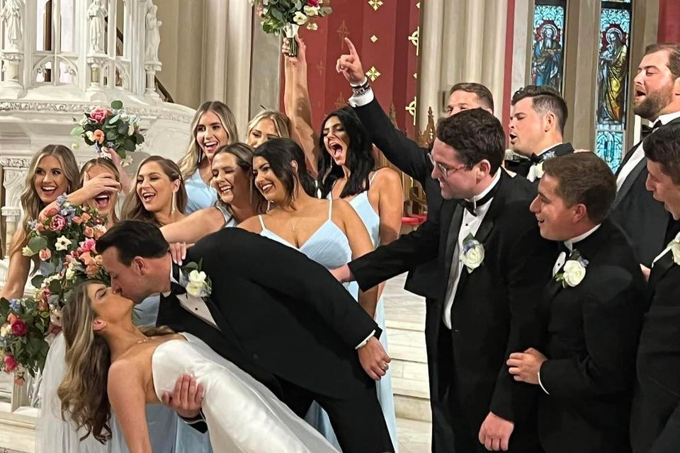 Bride and groom sharing a kiss while the wedding party cheers around them inside a church.