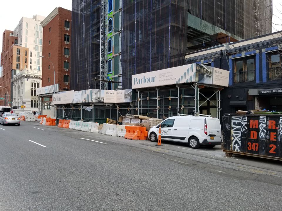 Printed banner panels wrapping a sidewalk shed on a Brooklyn corner