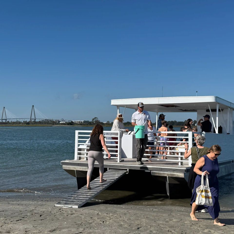 Guests stepping off the Roamer IV pontoon onto a Charleston harbor beach with the Ravenel Bridge in the background