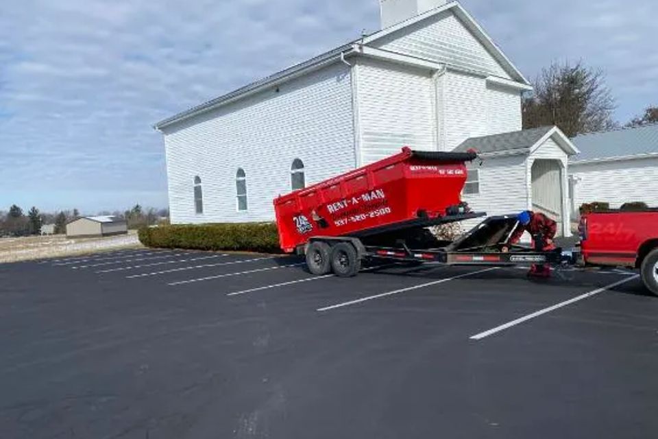 Rent-A-Man Dumpster Rentals truck unloading a red dumpster from a trailer.