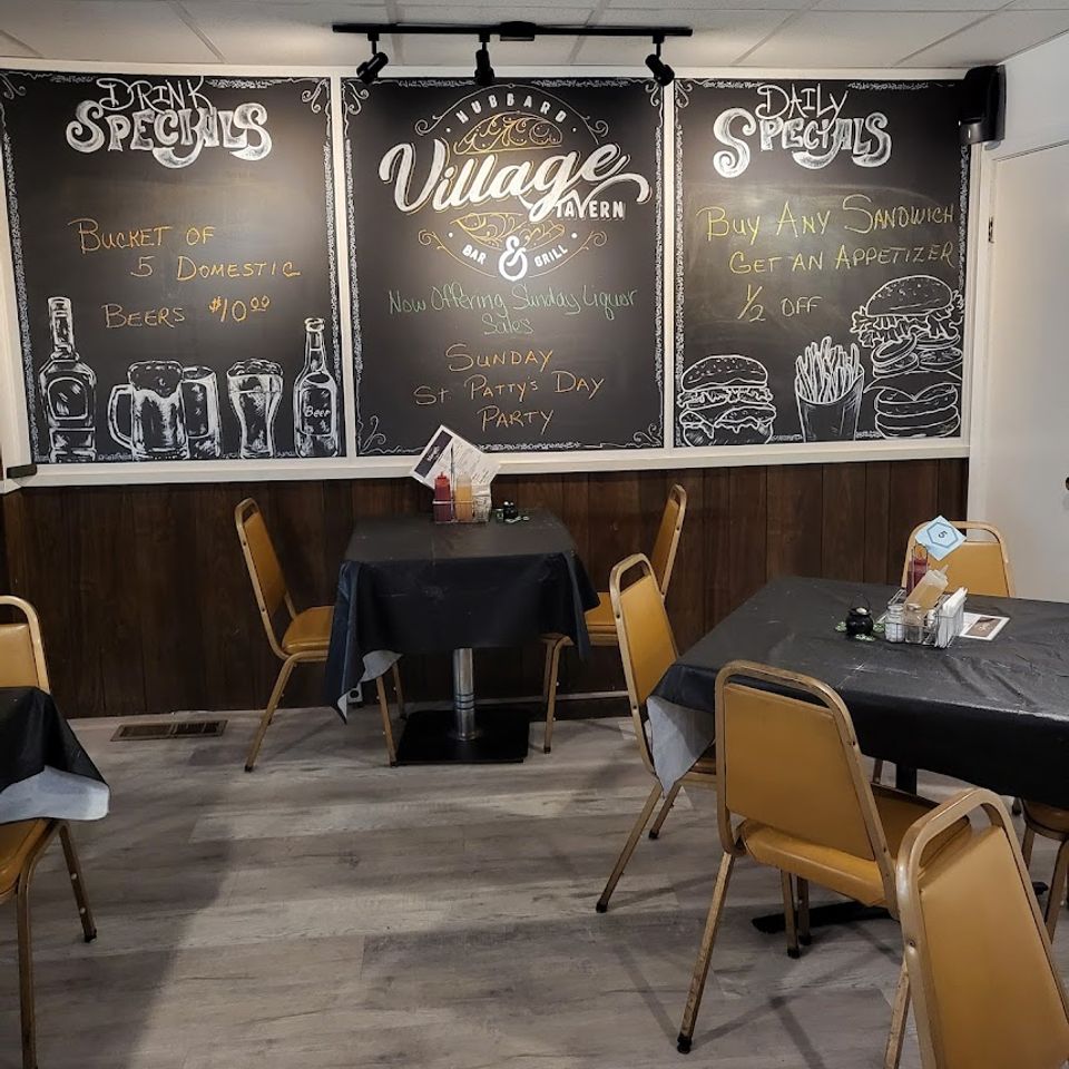 Dining area with tables and chalkboard wall showing Village Tavern drink and food specials