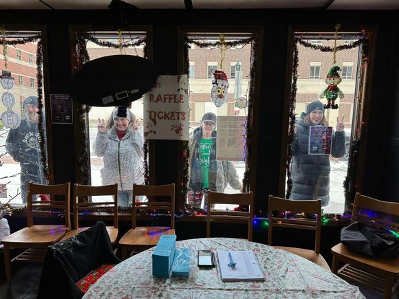 Attendees standing outside decorated windows during a holiday event, smiling and posing for a photo.