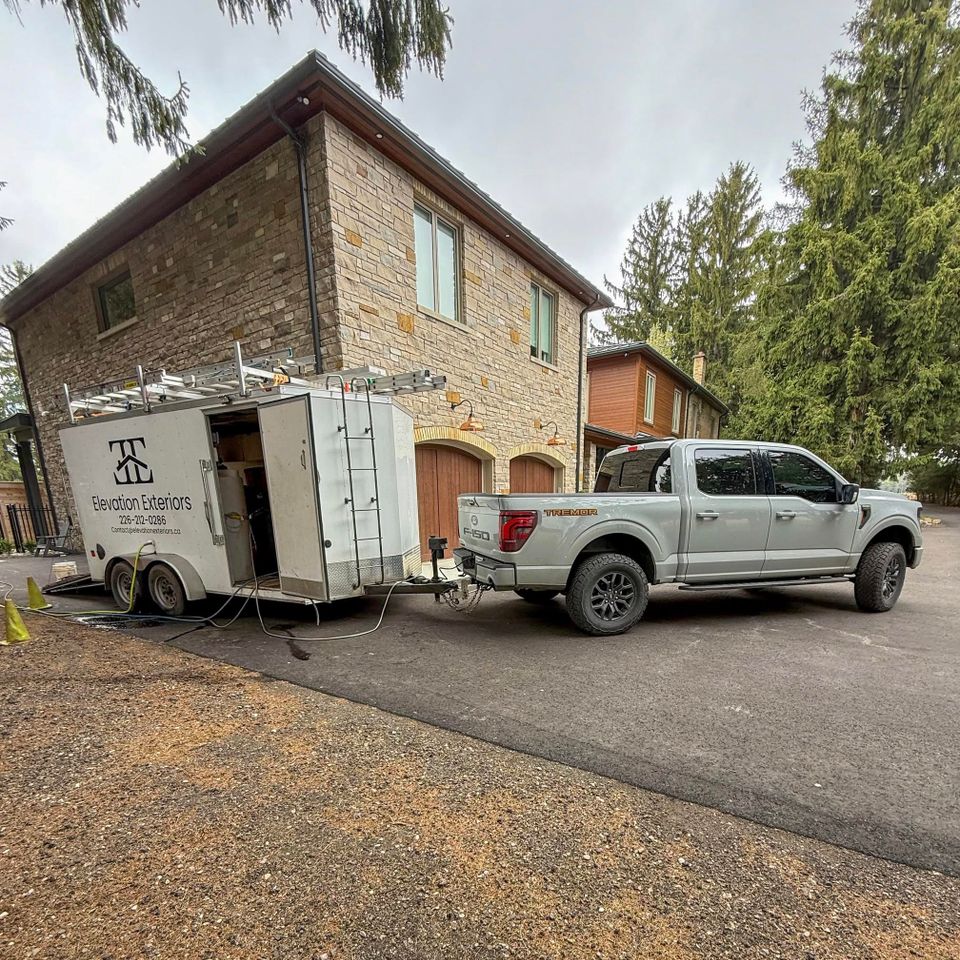 Elevation Exteriors trailer and truck set up with hoses at stone home for pressure washing in Tillsonburg