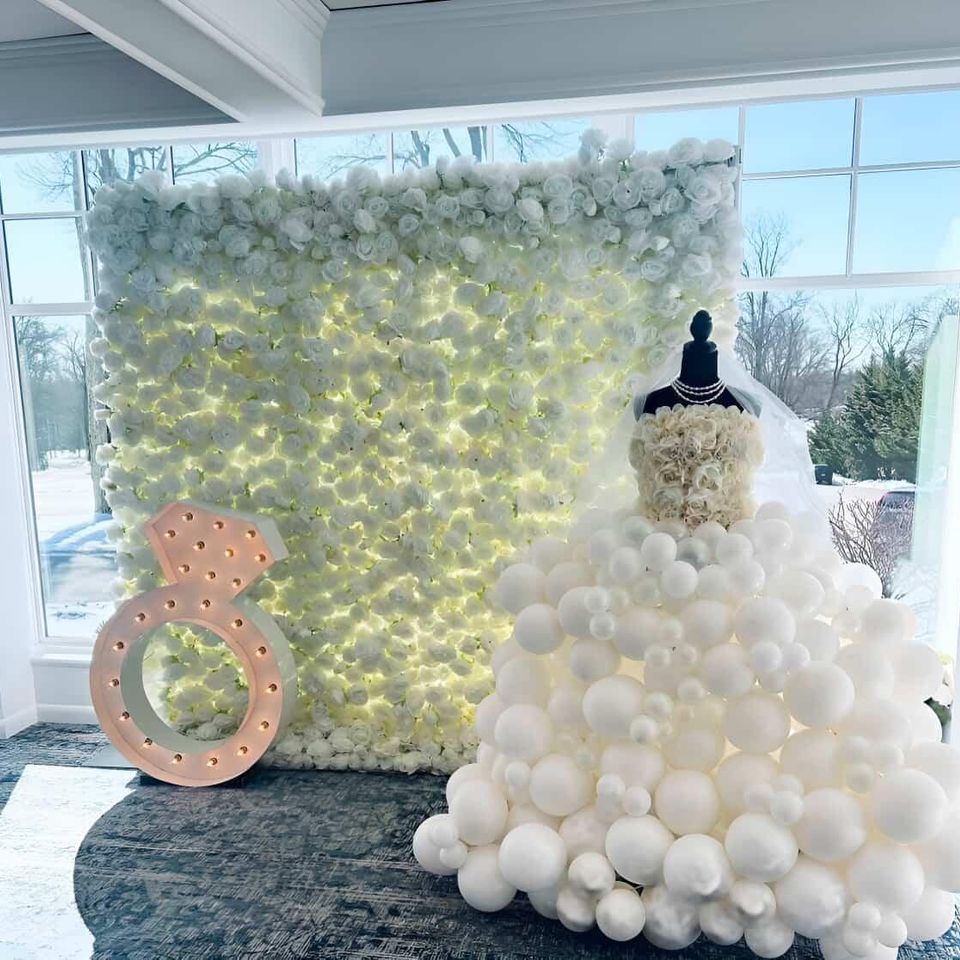 Elegant bridal shower balloon dress display with white floral backdrop and marquee engagement ring prop by Aldys Events