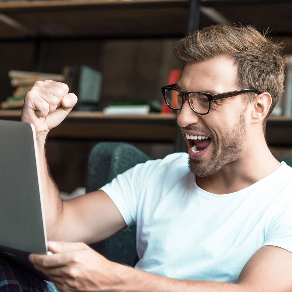 Man pumping his fist in celebration while looking at a laptop