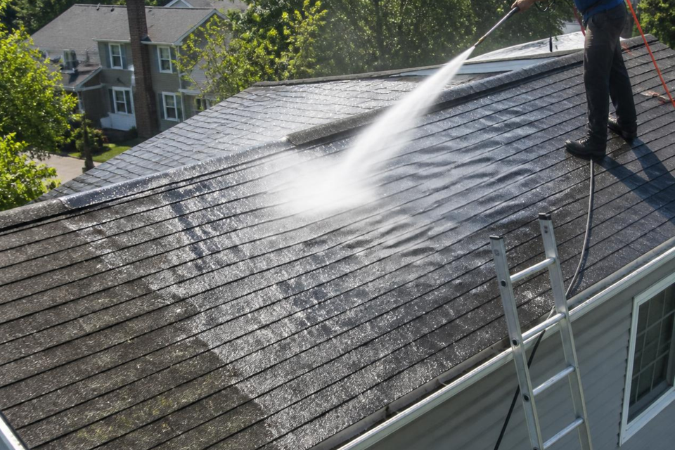 Cleaning a residential roof with professional pressure washing equipment to remove dirt and other surface buildup.