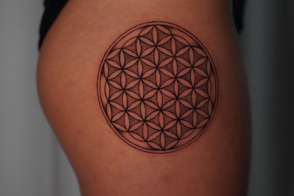 Image of a round black and grey tattoo with flowers connected at the petals to each other, very detailed