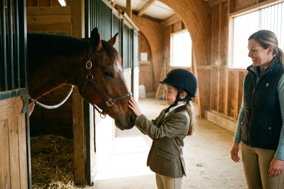 Child in riding gear petting brown horse in stable with instructor smiling