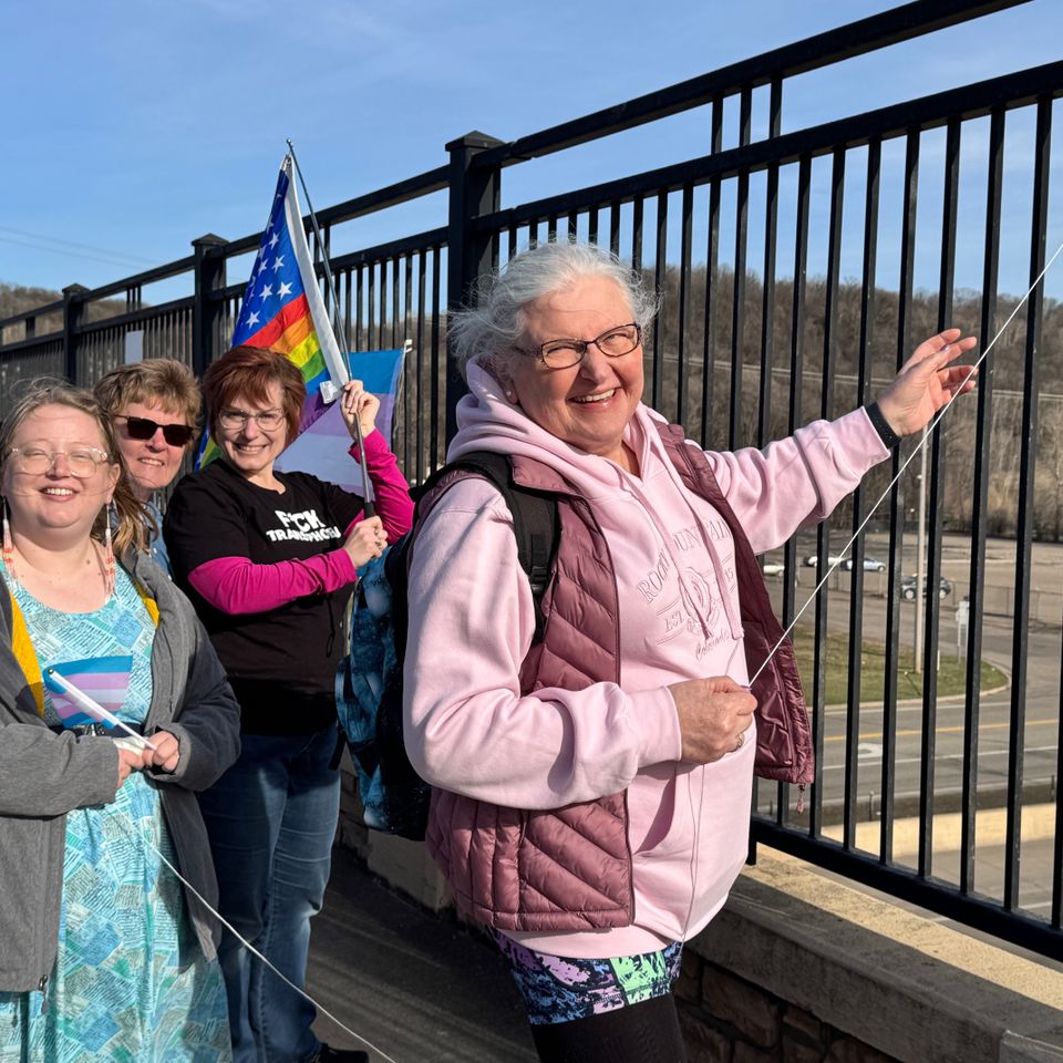 4 people standing on an overpass with trans day of visibility signs