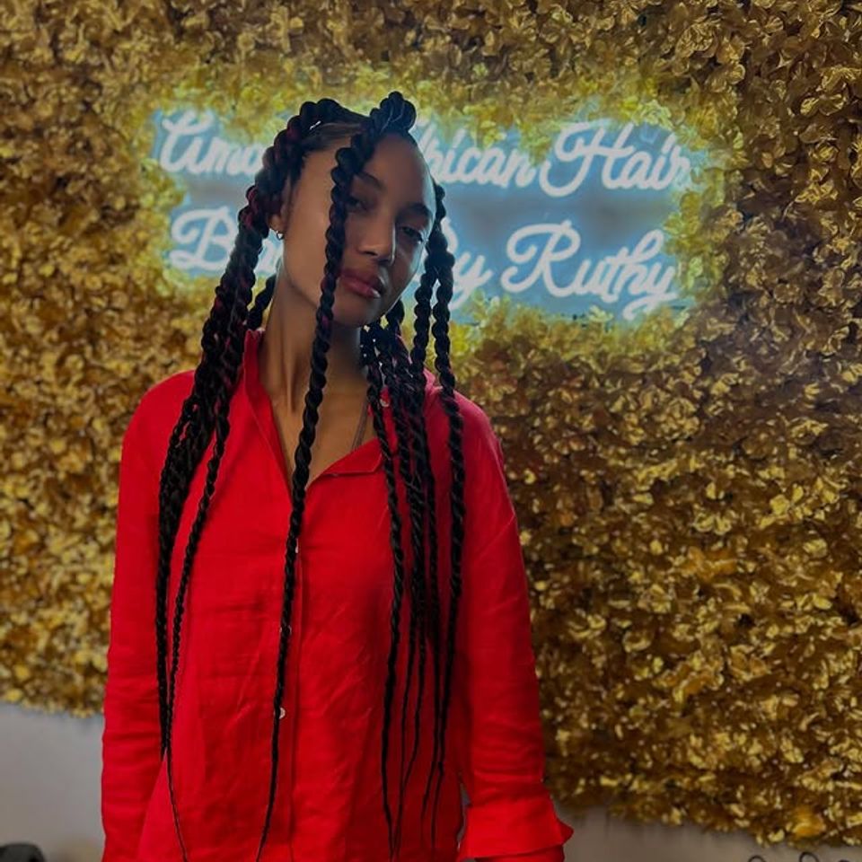 Long jumbo box braids styled in front of the salon neon sign in Los Angeles CA
