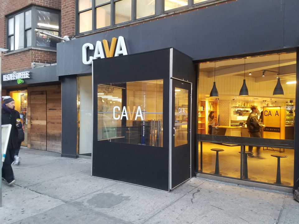 Black framed winter vestibule with a branded front panel enclosing a lit restaurant entrance on a city sidewalk