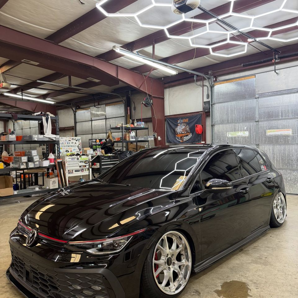 Lowered black Volkswagen Golf GTI with tinted windows under hex lighting in the tint shop