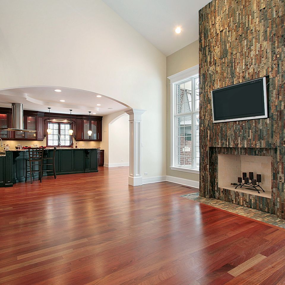 Great room with rich cherry-toned hardwood flooring, stone fireplace, and open kitchen