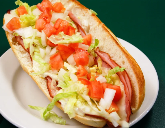 Sub sandwich topped with lettuce, tomatoes, onions, and sliced meat at Cocca’s Pizza.