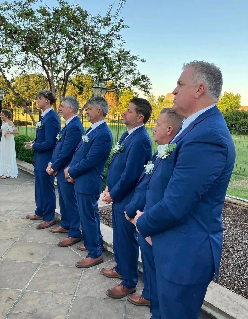 Groomsmen wearing tailored blue tuxedos from New Orleans Tuxedo Inc. at an outdoor wedding ceremony.