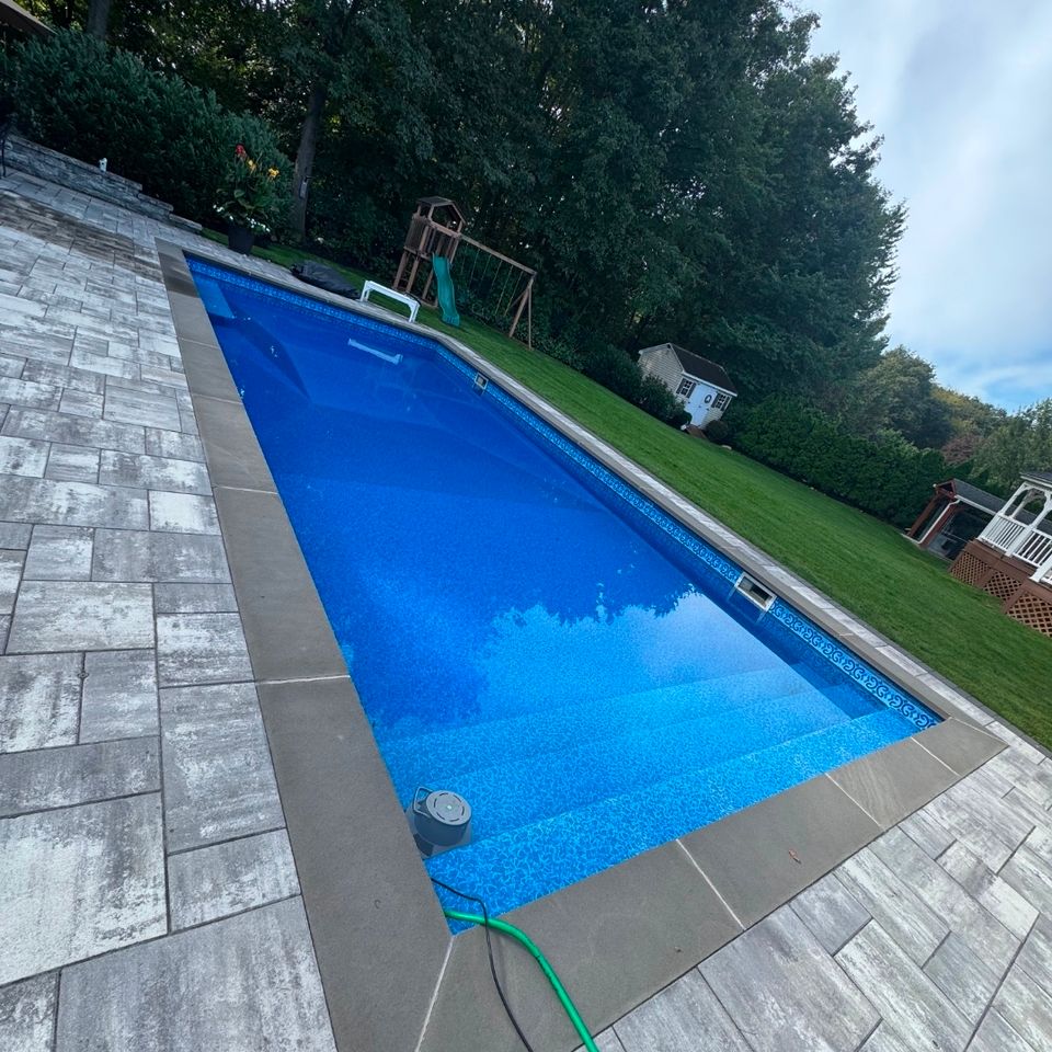 Long rectangular inground pool filled after a liner replacement with gray paver deck in Long Island NY