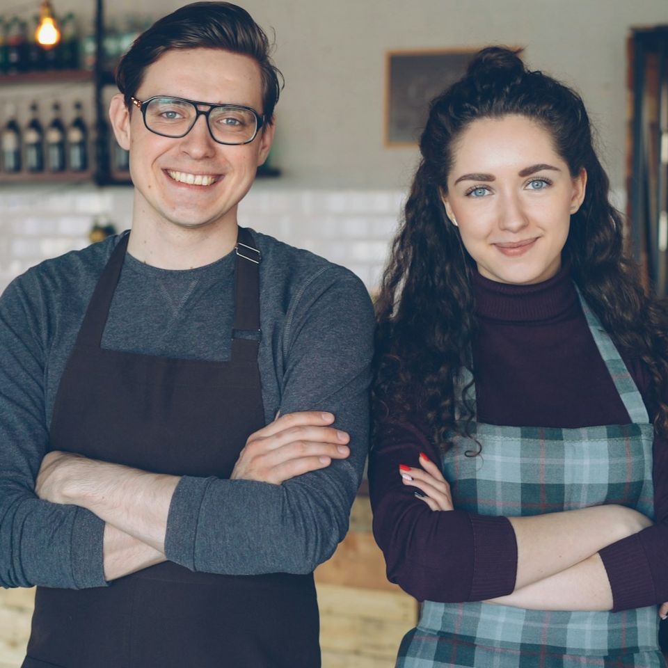 2 happy business owners with their arms crossed while standing in their shop