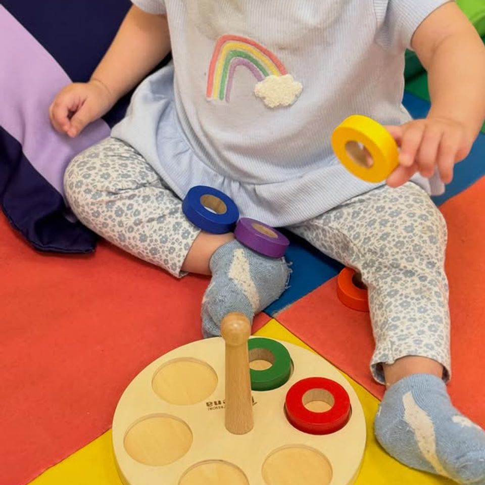 Baby placing a wooden ring on a stacking peg toy during toddler daycare playtime in Palmdale CA