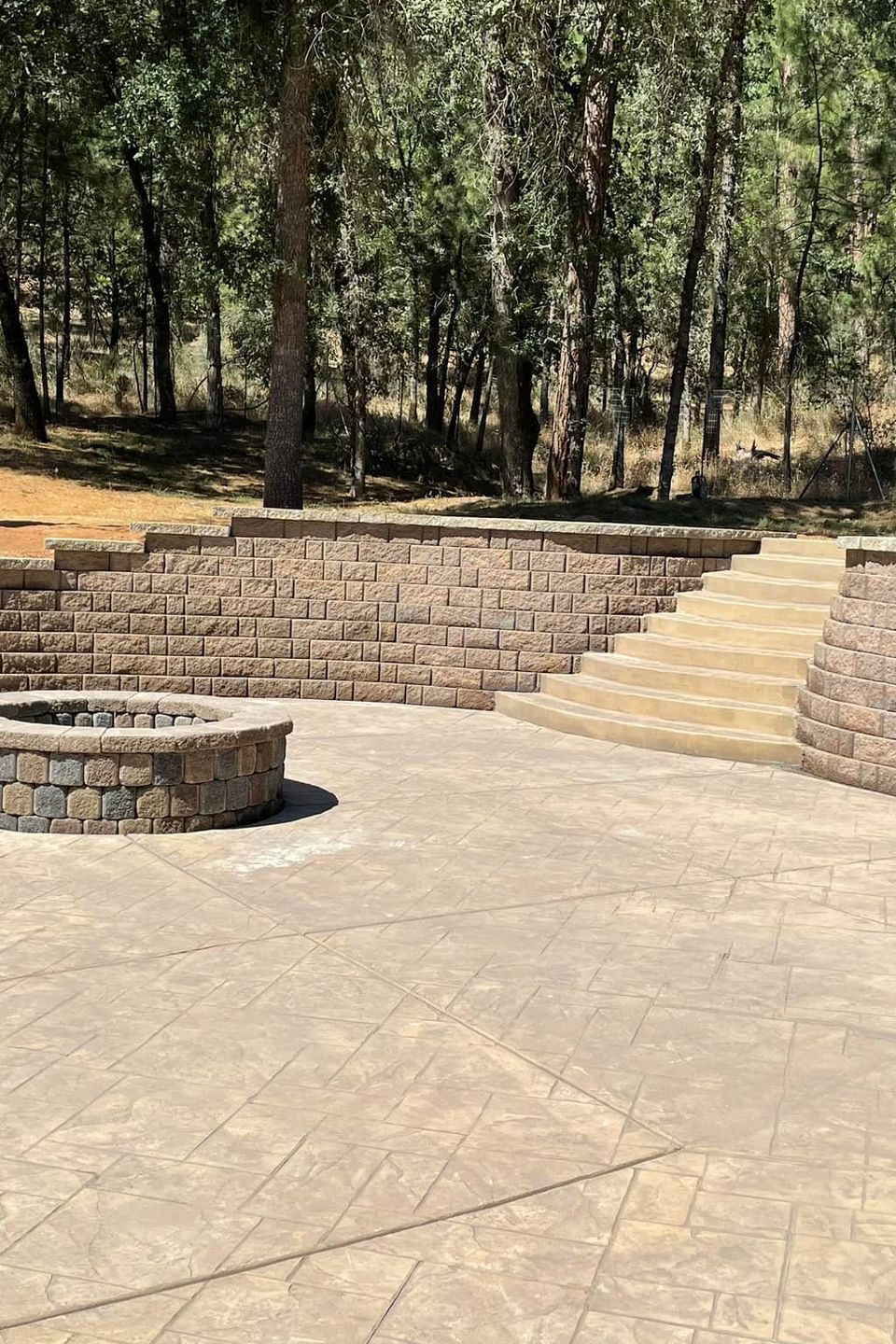 Modern backyard retreat featuring a custom stone fire pit, stamped concrete patio, and a tiered block retaining wall with integrated stairs, professionally designed for outdoor entertainment in Northern California