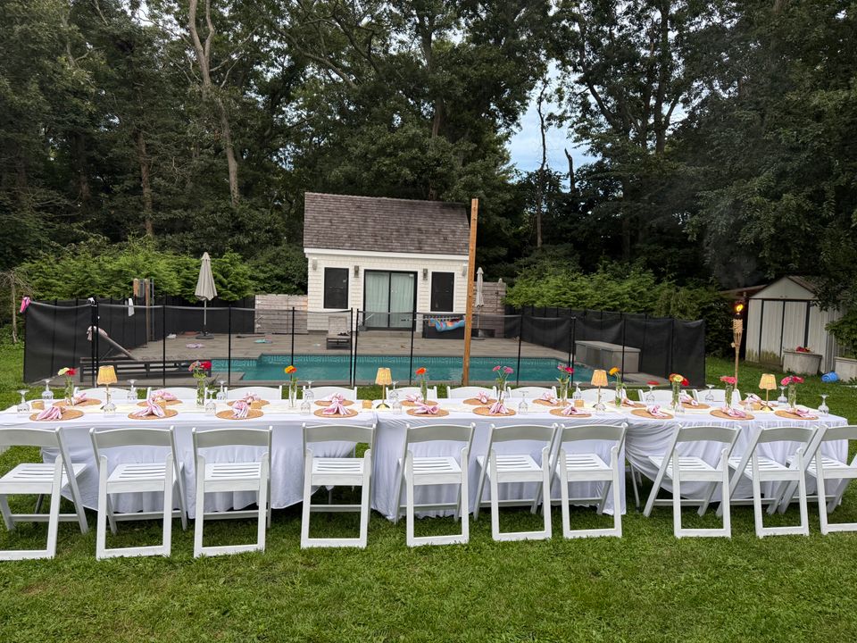 Long poolside banquet tables with pink napkins and zinnia bud vases in a Hamptons NY backyard