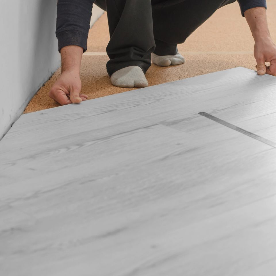 Flooring installer setting light gray laminate planks over underlayment in a bedroom