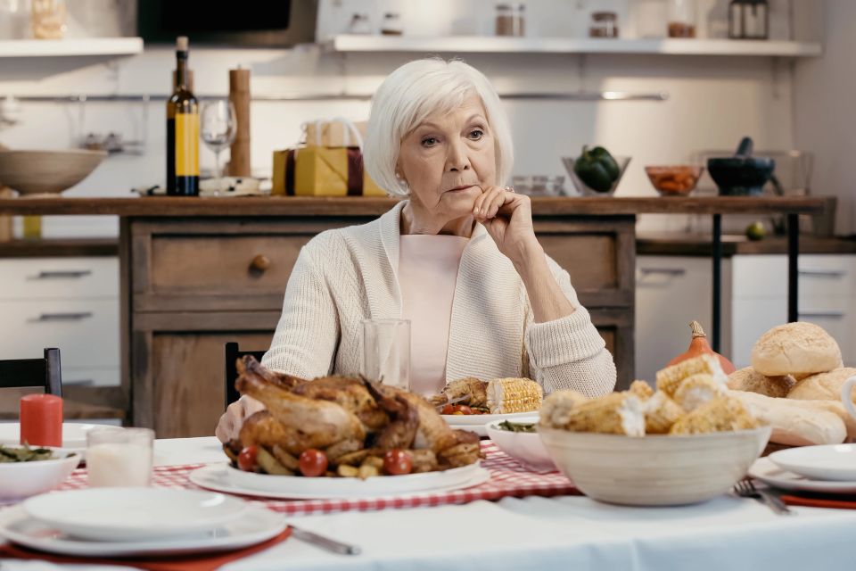 Lonely and thoughtful senior woman sitting near thanksgiving dinner served on table in kitchen