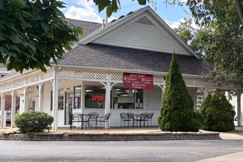 Cocca’s Pizza Poland, Ohio storefront featuring a white building with wraparound porch seating, landscaped grounds, and an illuminated open sign.