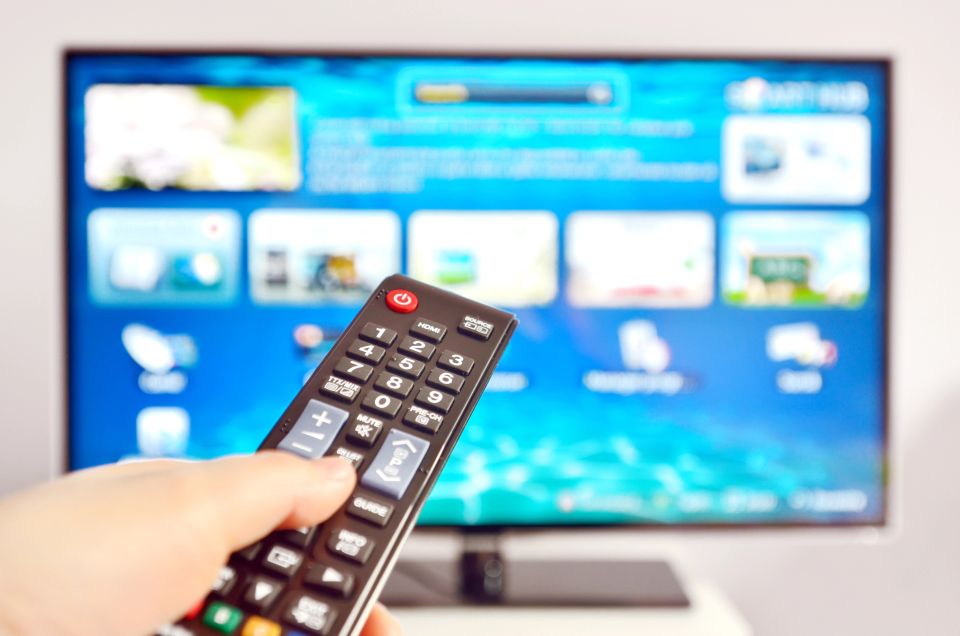 A stock image of a person using a smart TV remote with a modern living room in the background, used in a blog by Cannone Marketing.