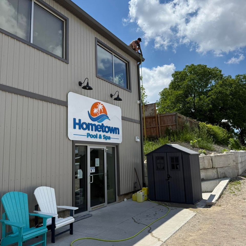 Technician cleaning gutters from roof edge of Hometown Pool and Spa commercial building in Tillsonburg ON