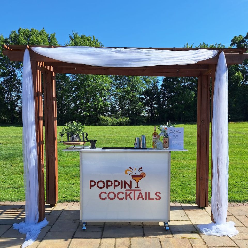 48-inch portable bar by Poppin Cocktails displayed beneath a pergola with beverage service essentials and a custom drink menu.
