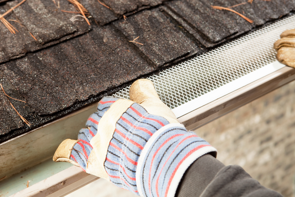 Technician installing a gutter guard system on a residential gutter to help prevent leaves and debris from causing clogs.