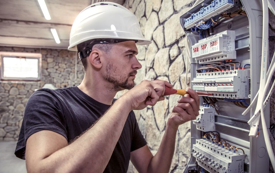 A male electrician works in a switchboard with an electrical connecting cable