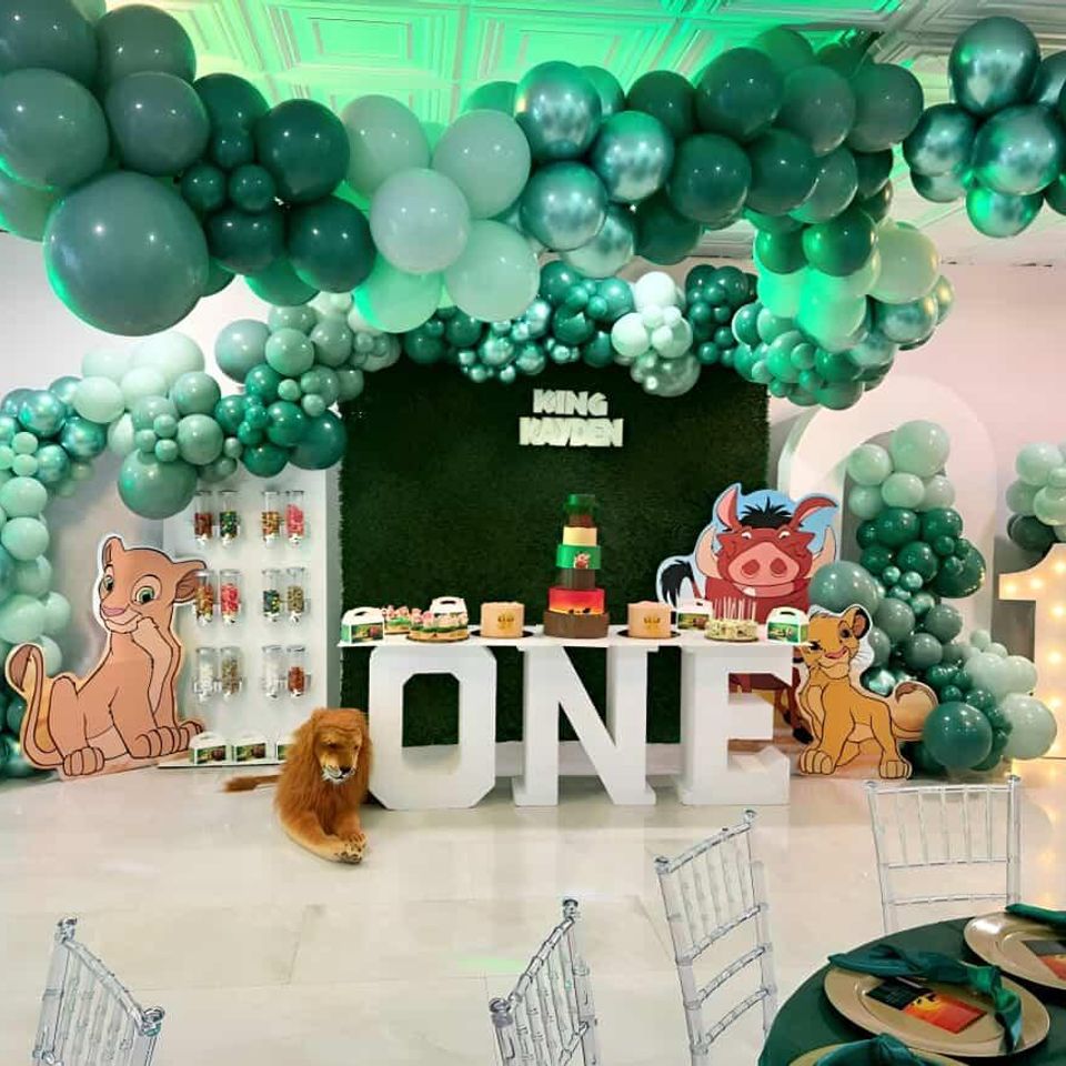 Lion King themed balloon backdrop in green with Simba, Pumbaa, and jungle décor for a first birthday celebration by Aldys Events