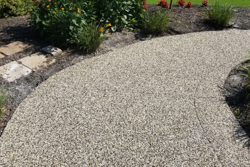 Curved decorative stone walkway bordered by landscaped flower beds, shrubs, and mulch.