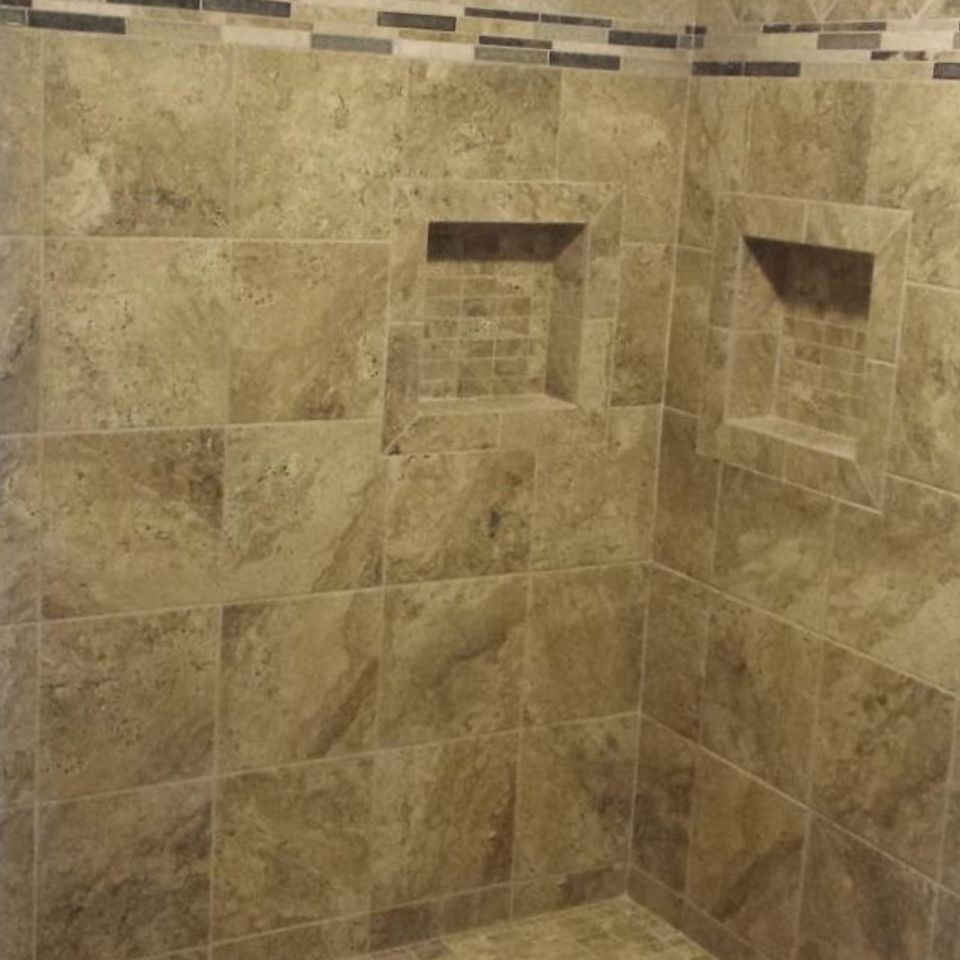 Beige tiled shower with built-in recessed niches and mosaic tile floor.