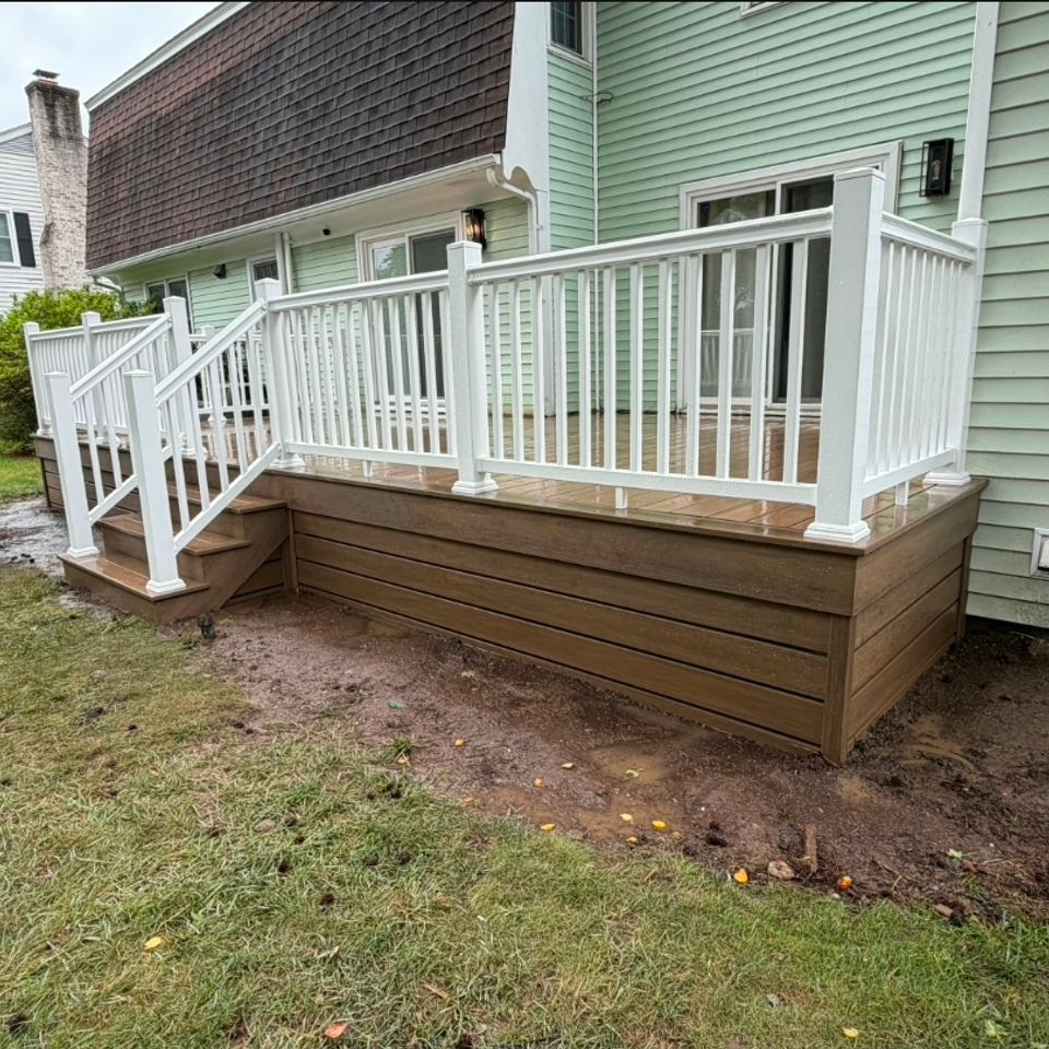 Composite deck with white vinyl railings and stairs behind green home in Virginia Beach VA