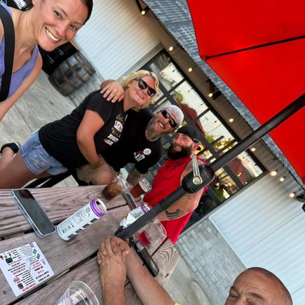 Group of event attendees seated around a table outdoors during a motorcycle community gathering.