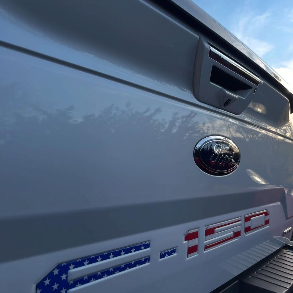 Close-up of a glossy white Ford F-150 tailgate with flag-pattern lettering after an exterior wash