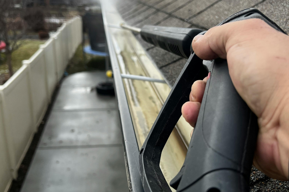 Close-up of a technician cleaning debris from a residential gutter using professional pressure washing equipment.
